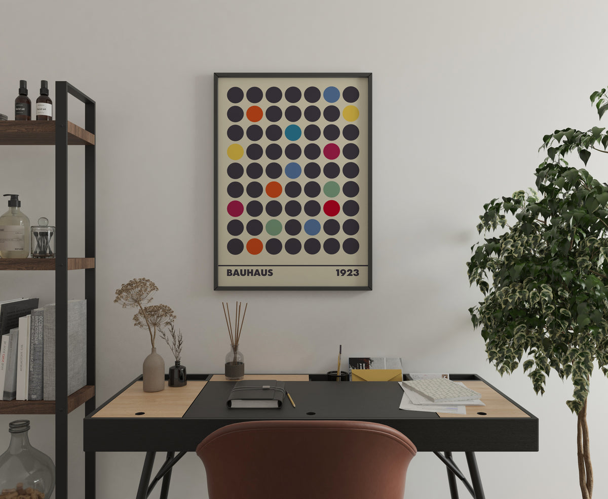 A Bauhaus 1923 poster with colored dots on a cream background hanging on a white wall above a desk.