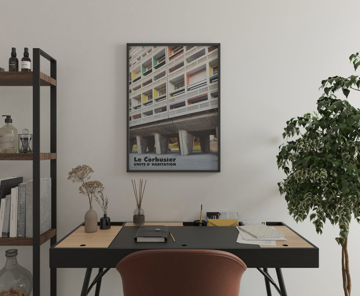 Le Corbusier UNITE D'HABITATION poster in a black frame hanging on a white wall above a desk.