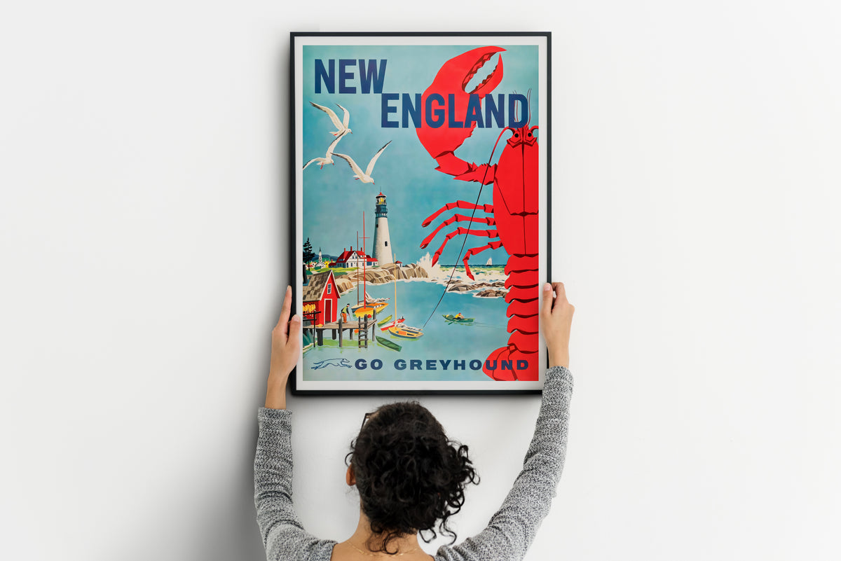 New England travel poster with lobster artwork and Go Greyhound text, shown being positioned on a wall
