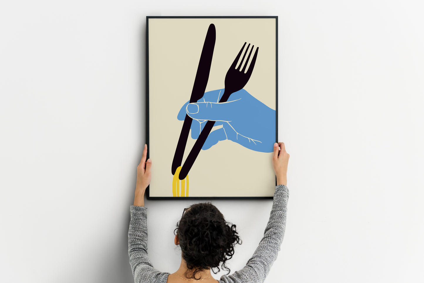 Person positioning a vertical noodles poster featuring a blue hand, fork, knife and yellow strands.
