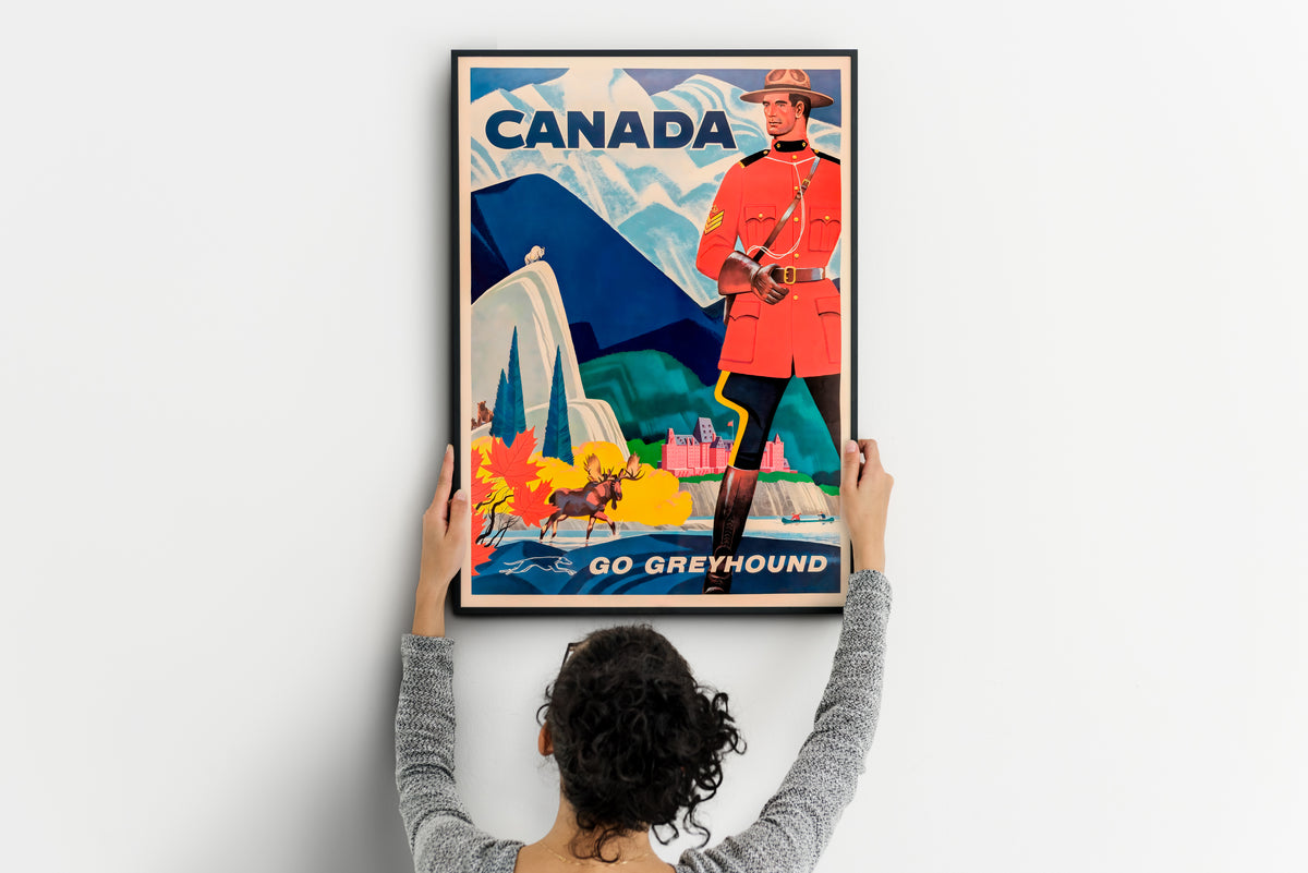 Canada travel poster with bold lettering, a Mountie and moose, shown being positioned on a wall