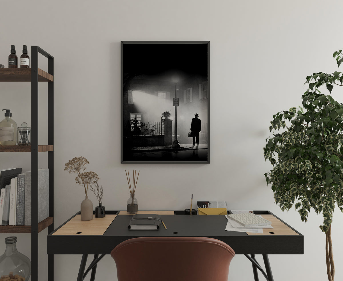 black and white Exorcist movie poster showing a solitary figure in a hat and coat standing on a wet street at night illuminated by a streetlamp casting a beam through fog with a building and windows in the misty background