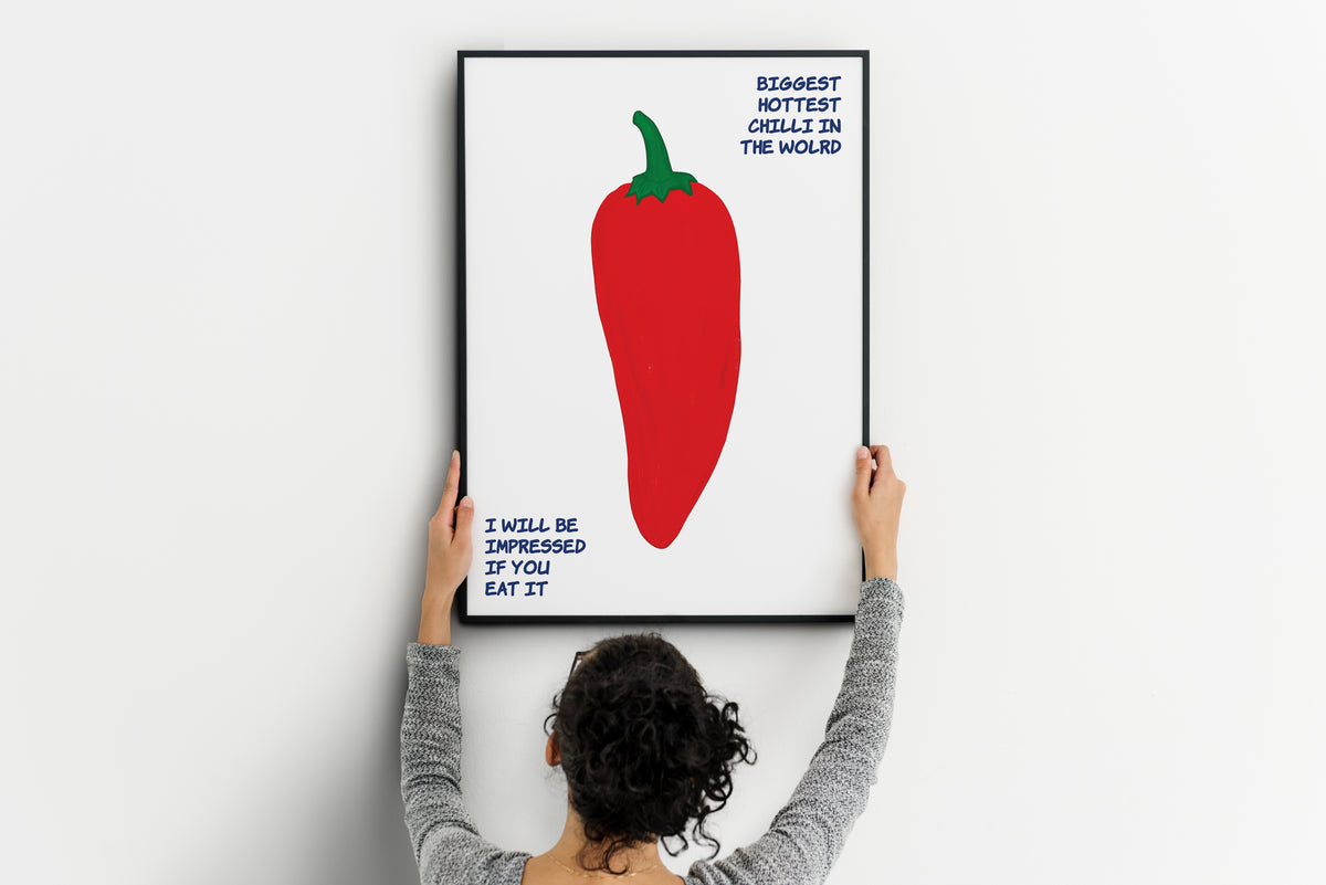 Giant red chilli food poster with green stem and hand-drawn blue text being positioned on a wall