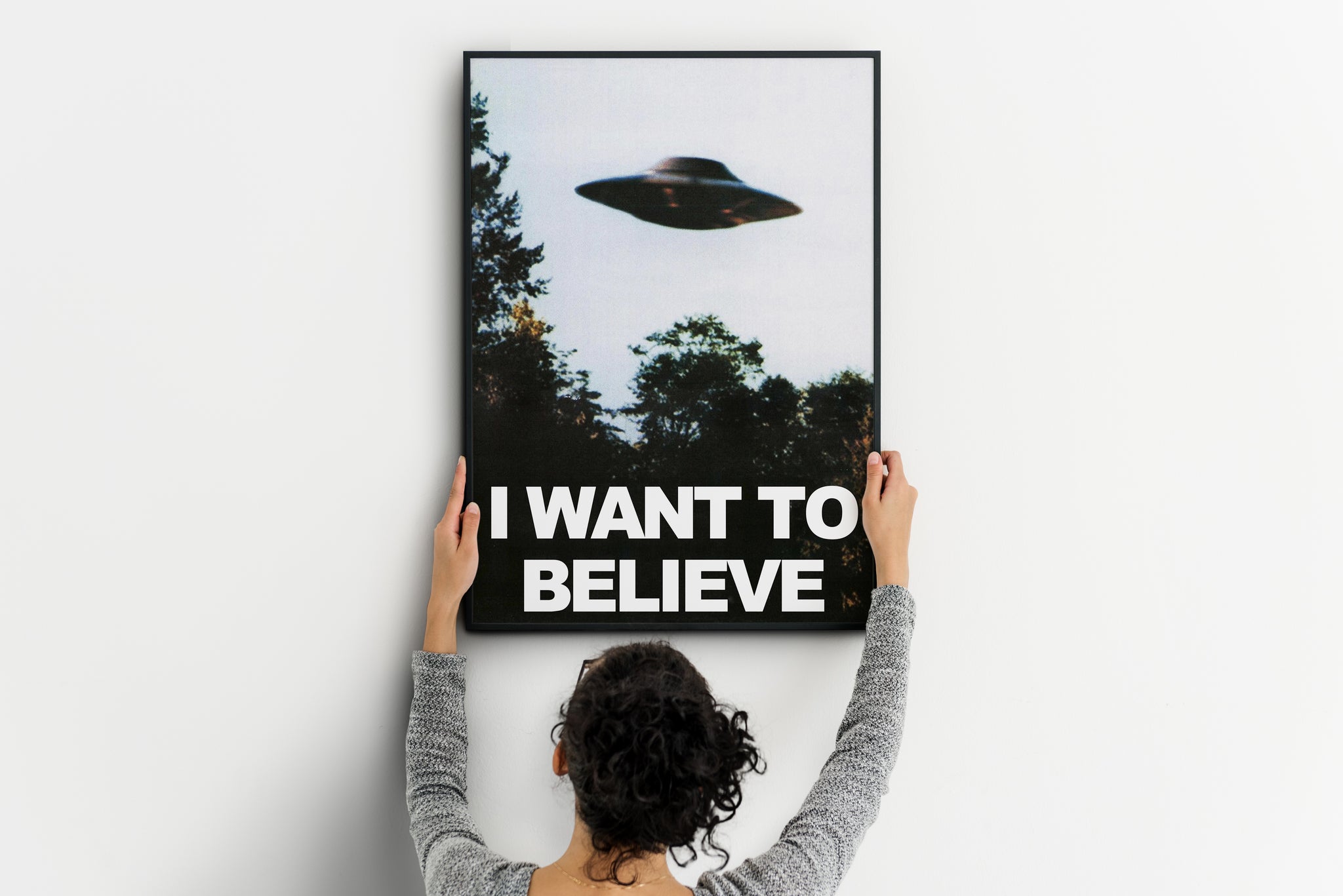 Person positioning an I Want to Believe UFO poster on a wall, showing the vertical format.