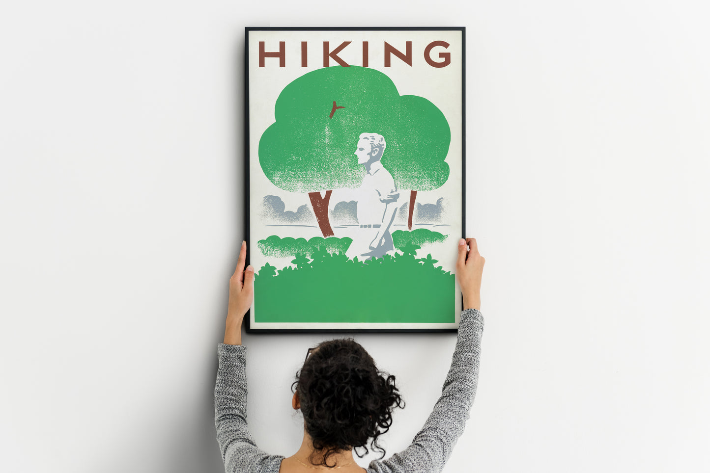 Large retro hiking print being positioned on a wall, showing a lone walker beneath green trees.