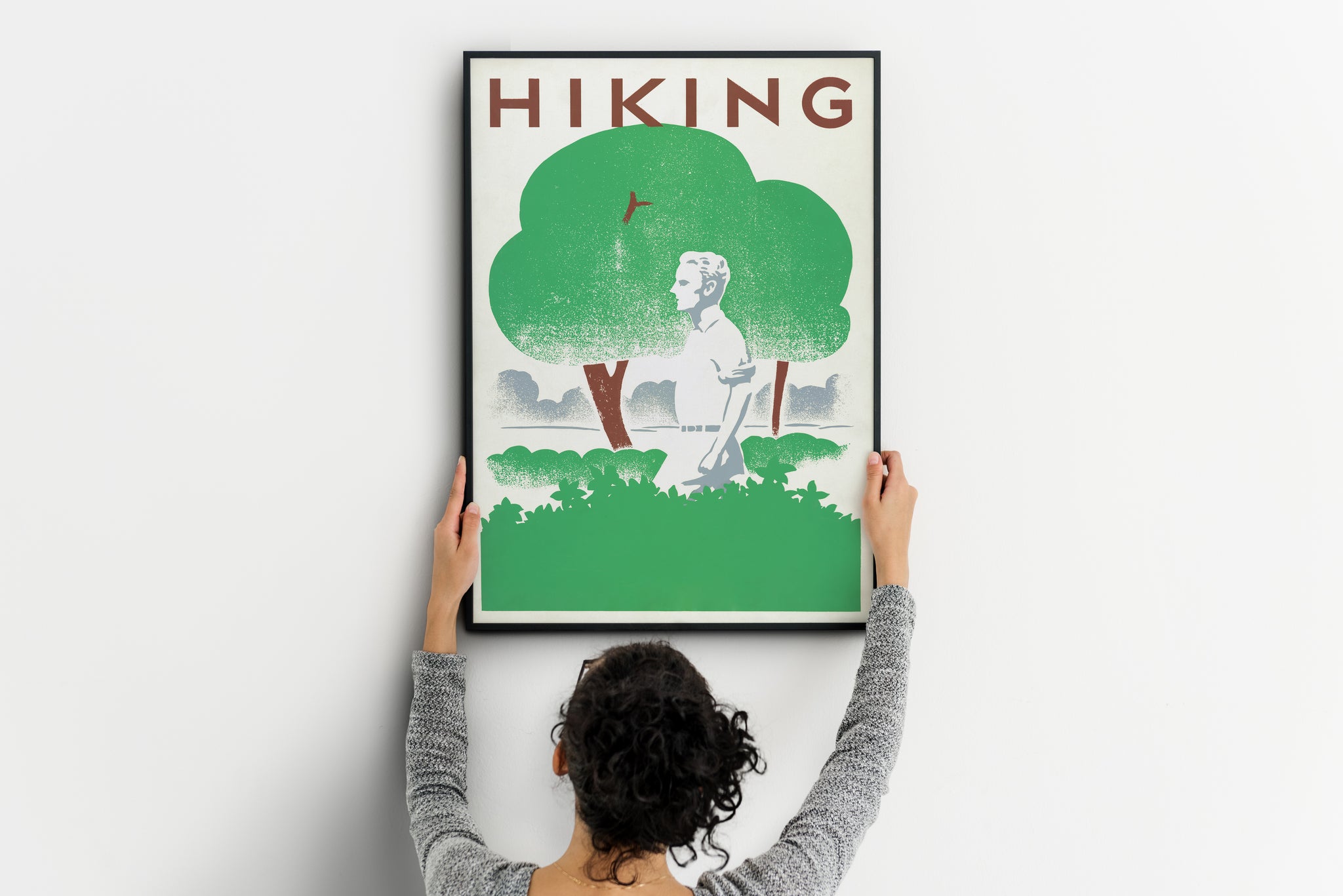 Large retro hiking print being positioned on a wall, showing a lone walker beneath green trees.