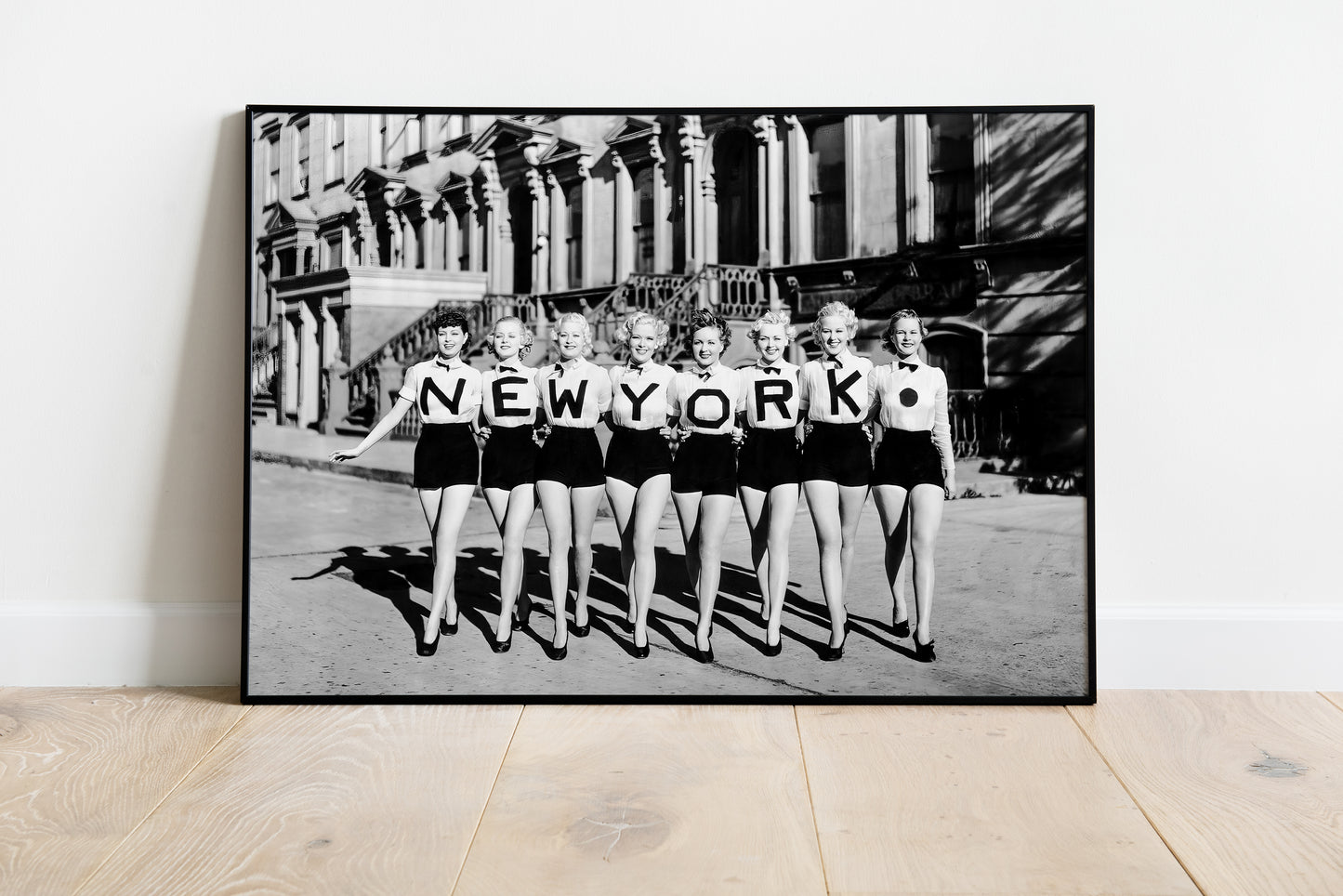 New York poster showing eight women in matching outfits with letters spelling NEW YORK in a black-and-white street photo.