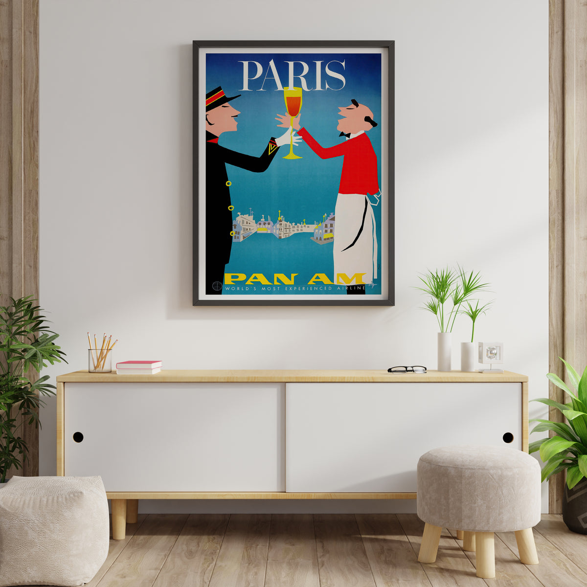 Pan Am Paris travel poster with toasting figures and blue graphic artwork shown in a living room.