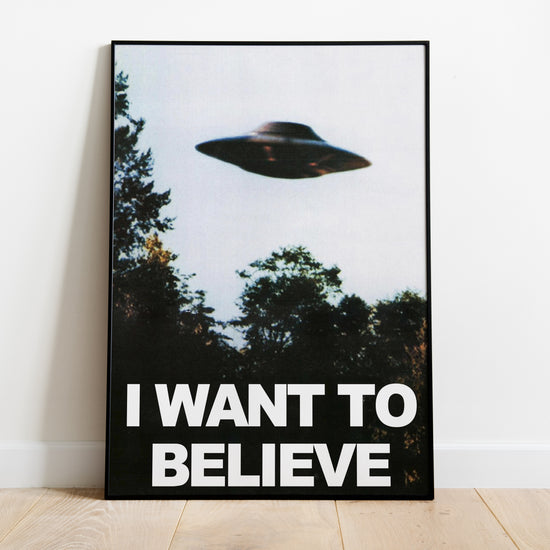 I Want to Believe UFO poster with a flying saucer above trees, shown in a moody living room interior.
