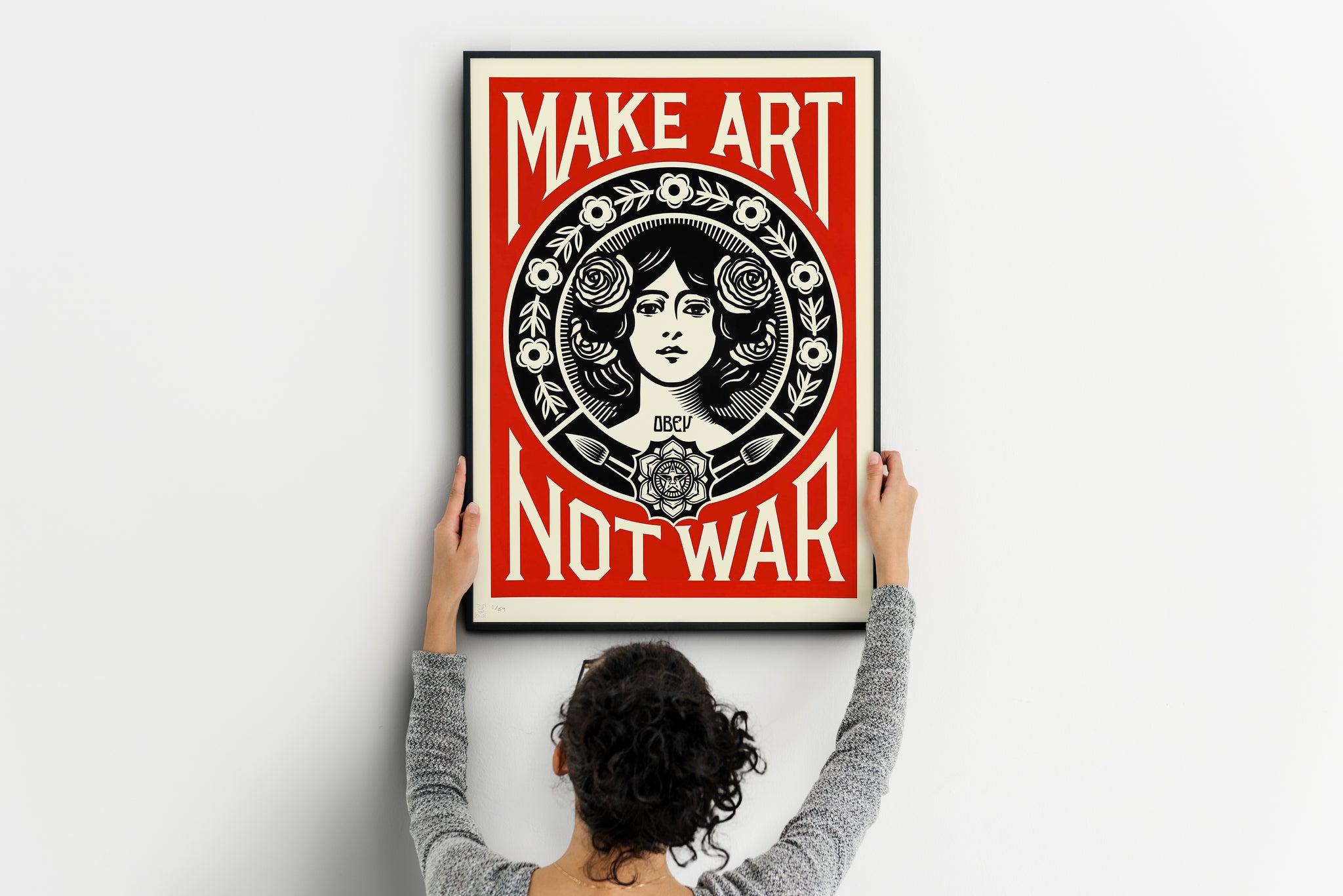 Person positioning a vertical protest art poster featuring a woman, roses and Make Art Not War text.