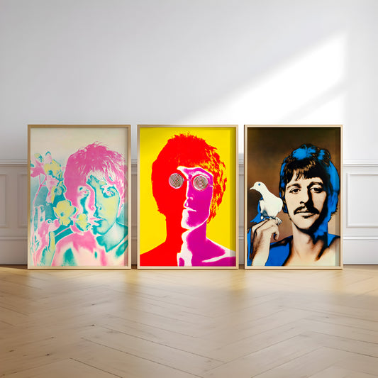 Three framed pop-art portraits of Beatles members John Lennon, Paul McCartney, and George Harrison displayed side-by-side on a light wood floor against a white wall.